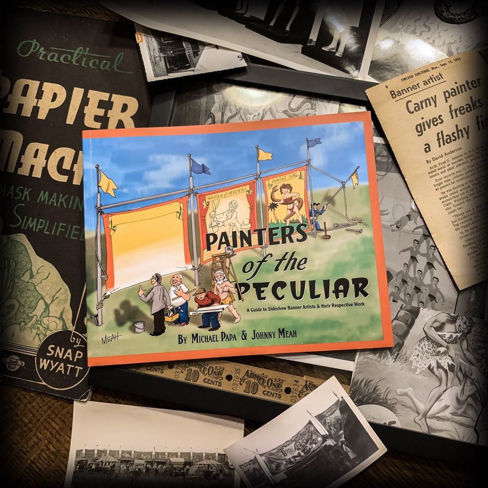 Painters of the Peculiar book by Michael Papa and Johnny Meah, shown on a table with vintage sideshow photos, Snap Wyatt's papier-mâché book, and a 1973 newspaper article on banner artist Fred Johnson